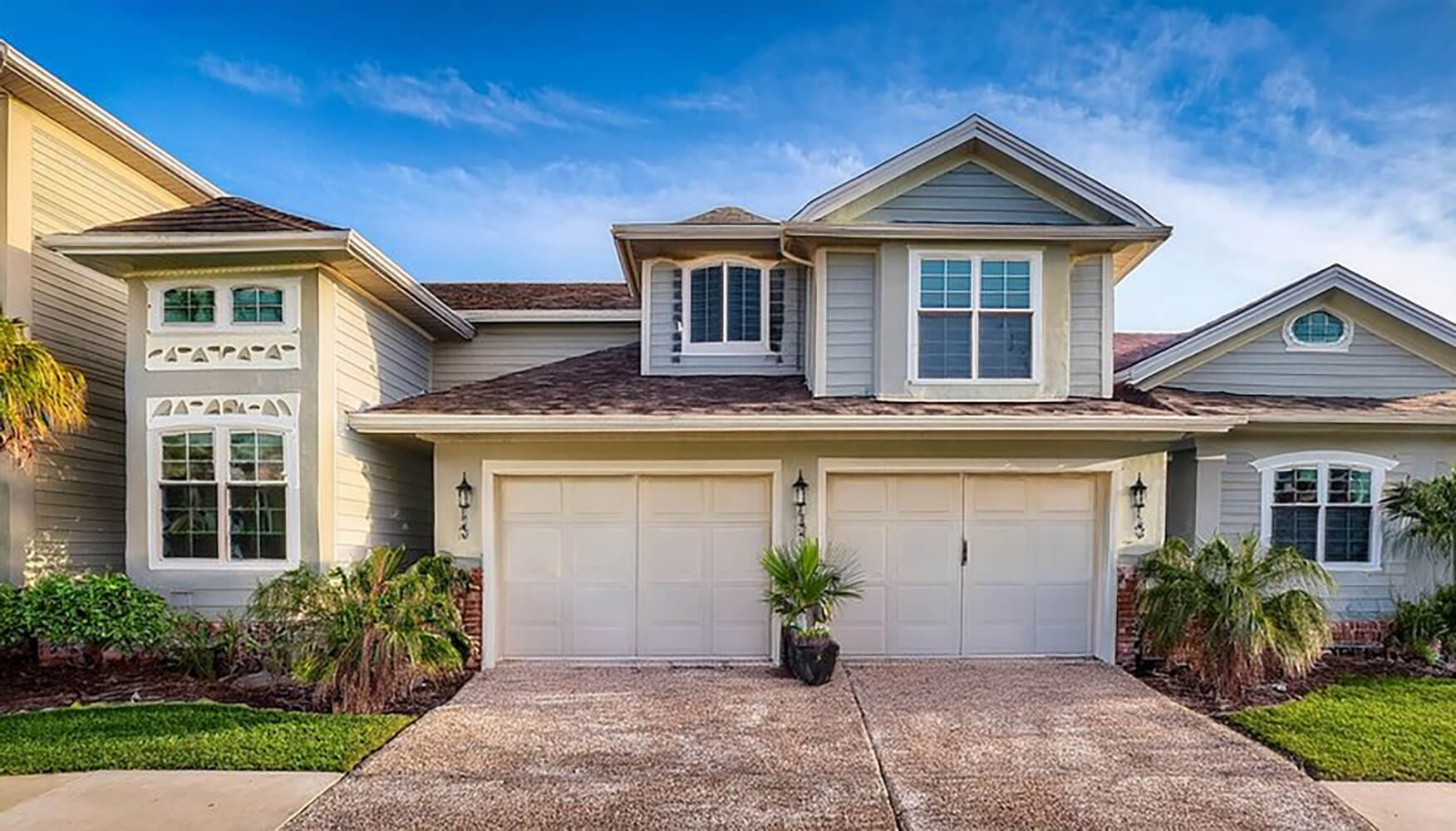 Freshly painted two-story Charleston SC home with cream siding, double garage, and tropical landscaping